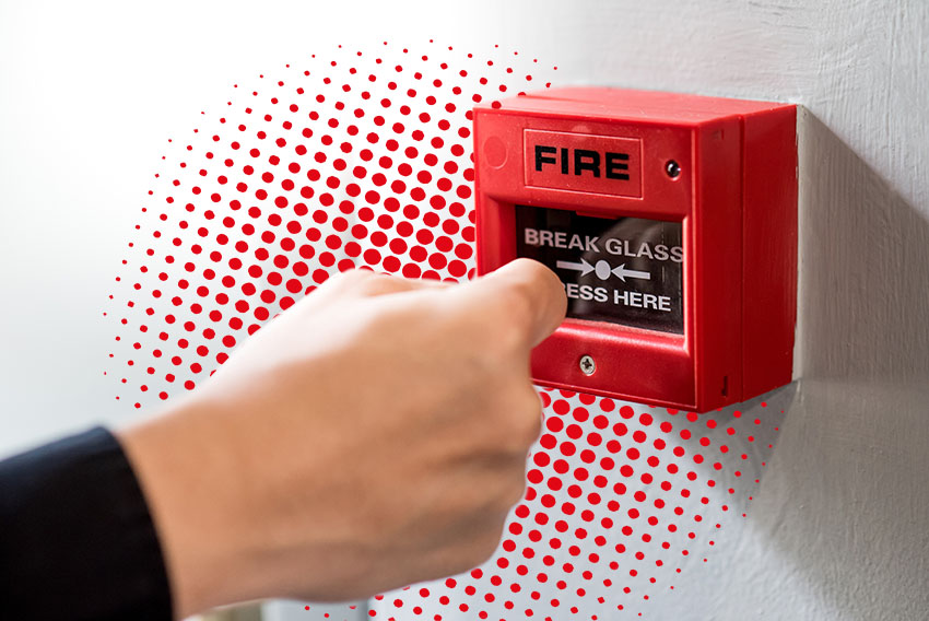 photographie d'une main appuyant sur le bouton d'alarme incendie. En fond il y a une trame de points rouges